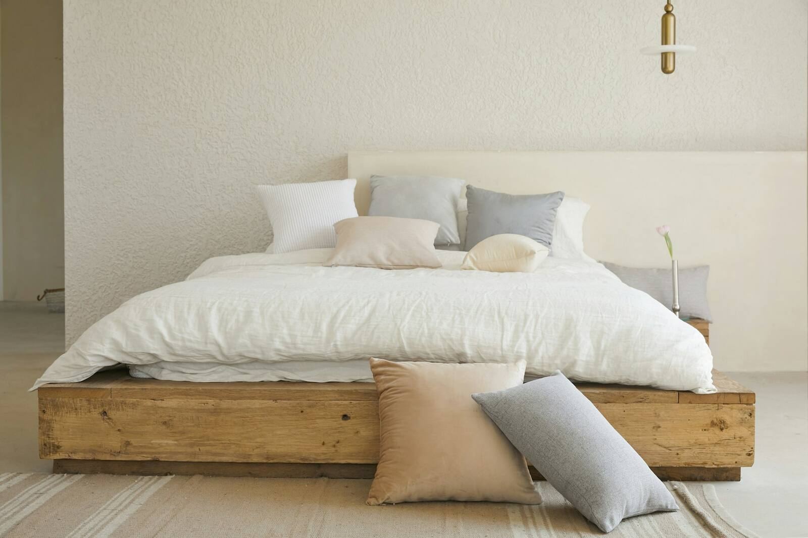 A calm bedroom with a wood bed frame, layered white linen and soft pillows