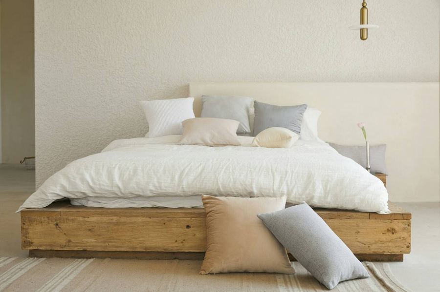 A calm bedroom with a wood bed frame, layered white linen and soft pillows