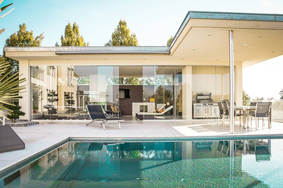 A covered outdoor living area with lounge chairs beside a long pool