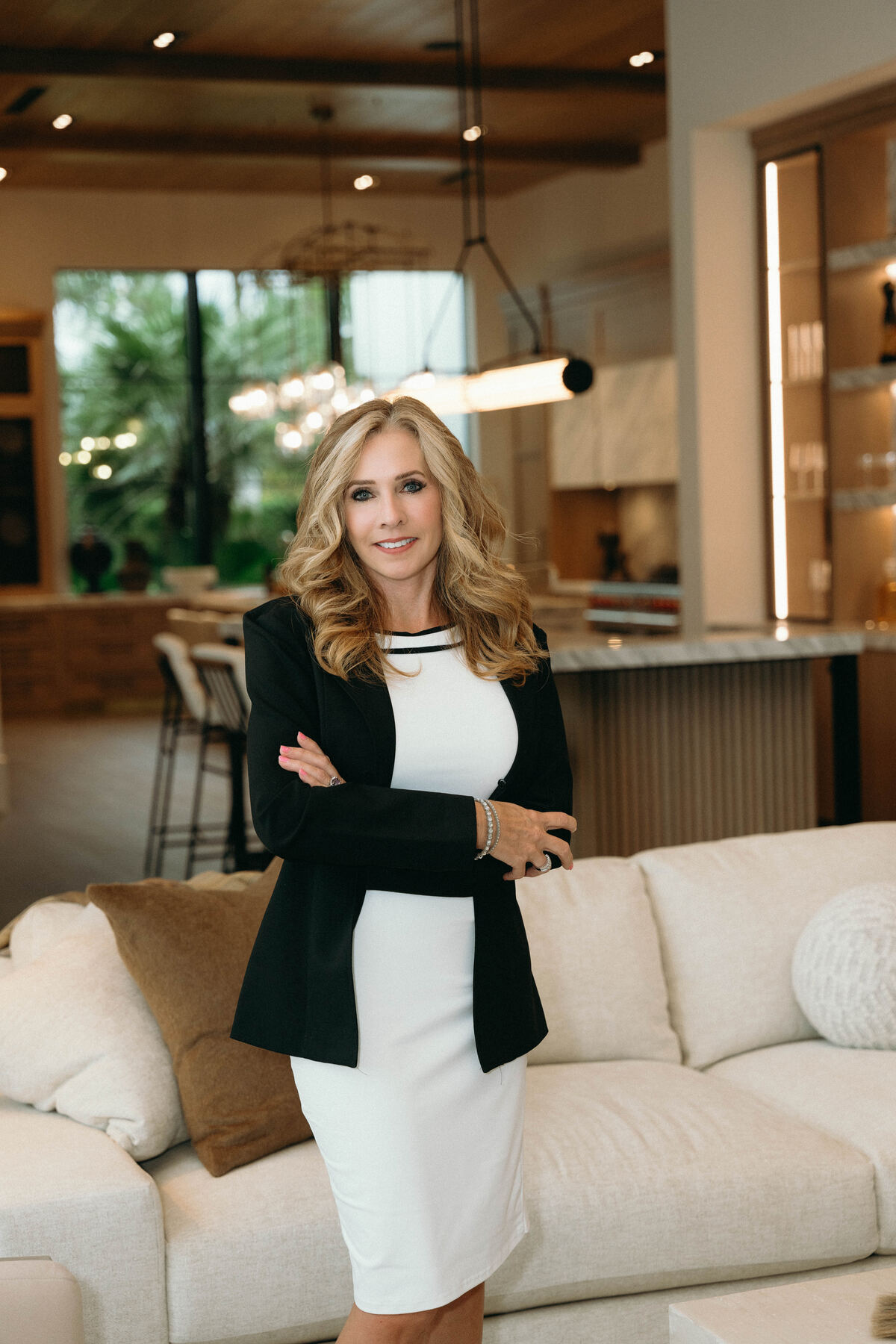 Diana Figurelli in a black blazer and white dress, standing in a light filled living room